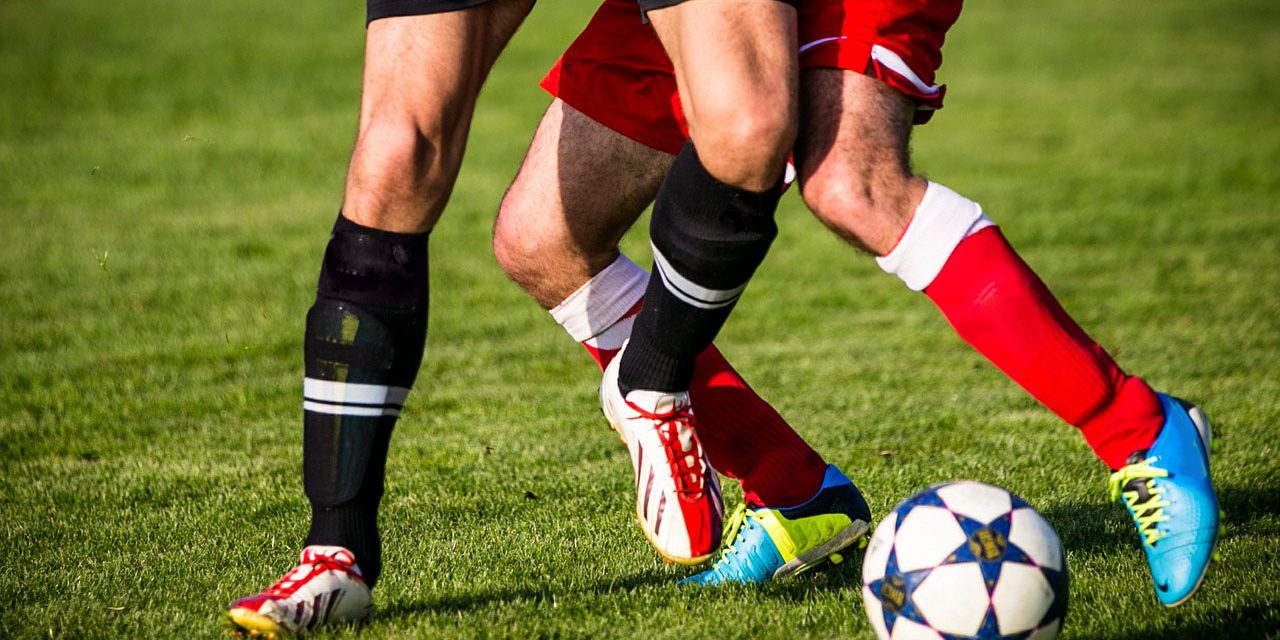 duas pessoas disputando uma bola de futebol em um gramado
